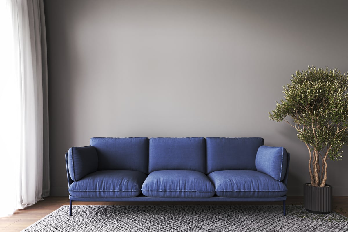 Modern livingroom mockup with dark blue sofa and green plant tree background. Modern rug, picture frame and empty gray wall. 3d rendering. High quality 3d illustration